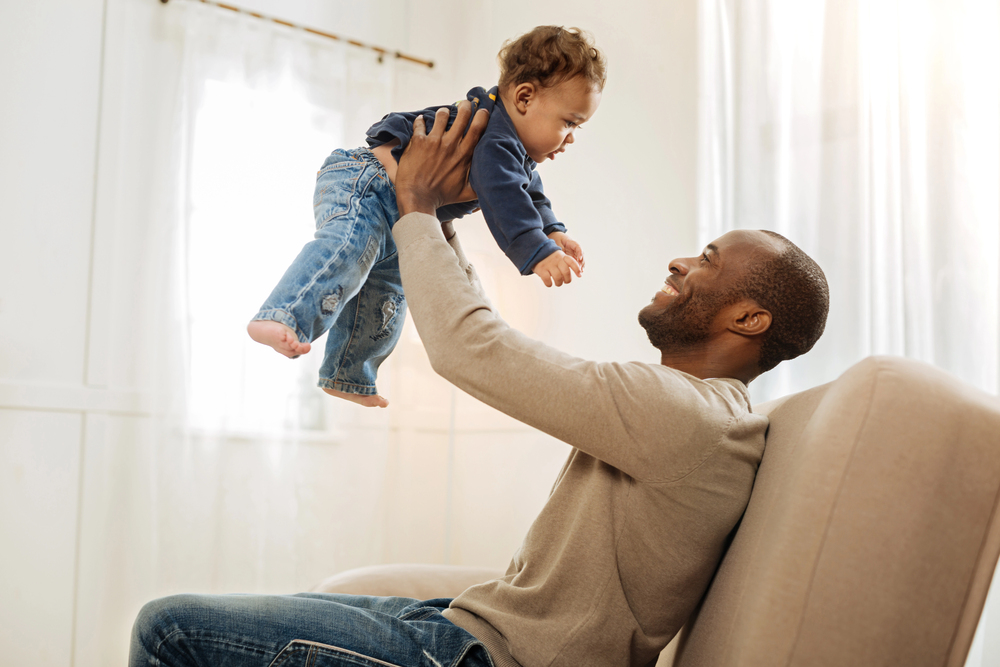Father lifting his young child in the living room, representing the importance of estate planning to protect minor children and plan for guardianship.