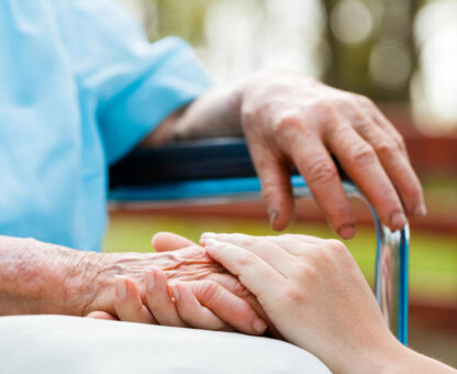 Caregiver holding elderly person’s hand in a supportive nursing home setting, representing long-term care planning and protection.