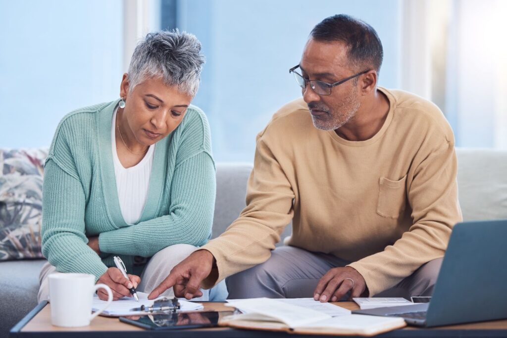 Couple reviewing financial paperwork at home with laptop, planning how to protect assets from nursing home costs.