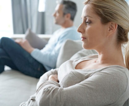 couple sitting apart on a couch with tense body language, illustrating the emotional challenges and financial decisions involved in divorce.