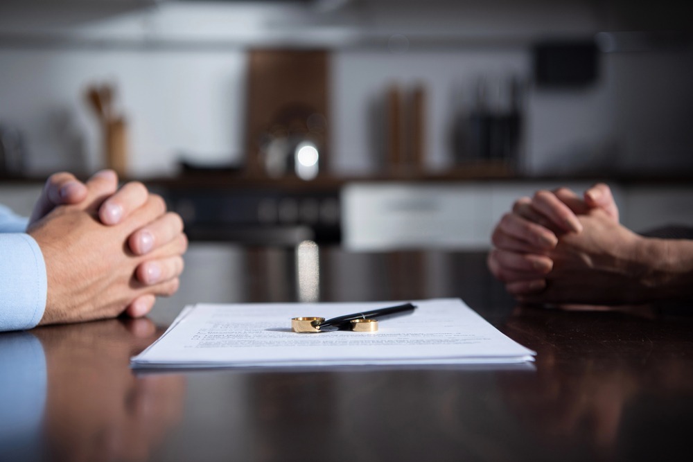 how to protect assets from divorce: two people sitting across a table with wedding rings resting on legal documents during a divorce discussion